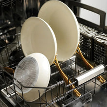 Cream fry pans with gold handles on dishwasher rack, three sizes
