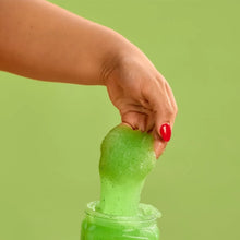 Hand scooping green shea sugar body scrub from a small jar