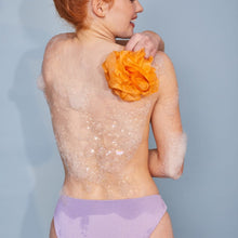 Foaming gel body wash with white suds on back skin, orange shower flower