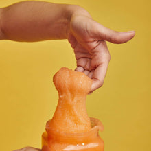 Shea sugar body scrub squeezed onto skin from an orange jar, exfoliating granules