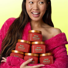 Watermelon body scrub jars stacked, shown beside a person wrapped in a pink towel.