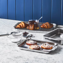 Stainless steel bakeware trays holding assorted baked goods for baking