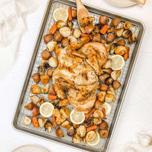 Steel roasting pan style baking sheet with ridged rack, holding roasted chicken
