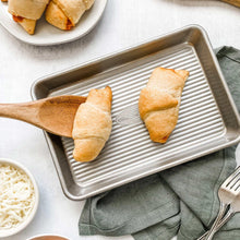 Ridged steel baking sheet with raised edges, holding two pastries