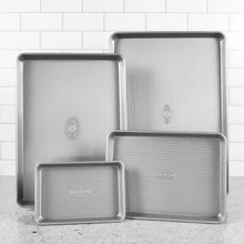 Stacked steel baking sheets set with ridged pattern and embossed seals, silver