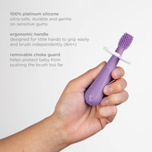 Purple toddler training toothbrush held in a hand with white removable guard and bristles
