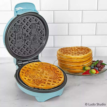Open light blue waffle maker with black plates and golden waffles cooking