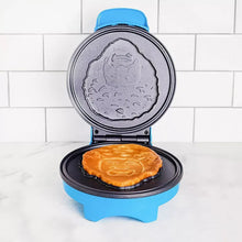 Blue waffle maker with open lid and circular plate, showing a cooked waffle