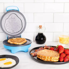 Blue waffle maker on kitchen counter with open lid and cooked waffle on plate