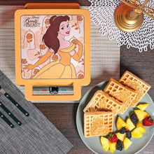 Yellow waffle maker lid shows Belle illustration; waffles and fruit on plate