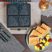 Gray waffle maker with character-pattern molds open, with waffles and fruit on plate