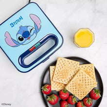 Blue Stitch waffle maker with open plates and two square waffles, strawberries nearby