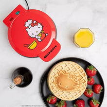 Red Hello Kitty waffle maker with lid open and waffle cooking plate