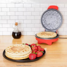 Red waffle maker producing round waffles with strawberries on a plate