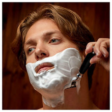 Safety razor with black handle during shaving, with white lather on face