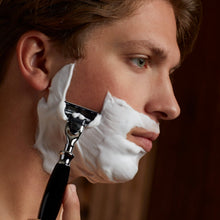 Safety shaving razor with black handle held during shaving with white lather