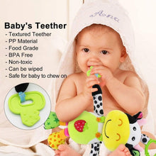 Baby holding a green cow teether toy with a plush cow hanging companion