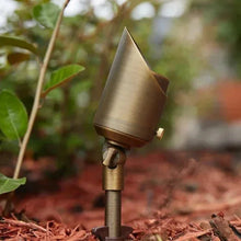 Brass low-voltage outdoor LED spotlight with angled head on ground