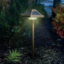 Illuminated brass solar path light stake in garden at night