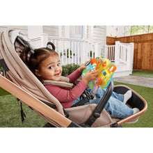 Child seated with baby driver toy in stroller, reaching toward the console buttons