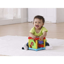 Baby playing with a colorful plastic activity cube toy on a floor mat