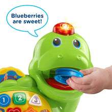 Close-up of green dinosaur toy mouth opening with hand holding a blue food piece