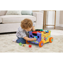 Green activity wagon toy with side openings, rolling wheels, and colorful shape blocks