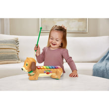 Dog xylophone toy as child lifts a green wand beside the yellow puppy