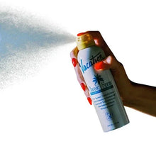 Sunscreen spray bottle held in hand with yellow cap and Vacation logo