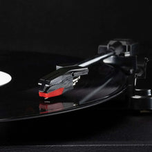 Record player tonearm with red cartridge on spinning black vinyl