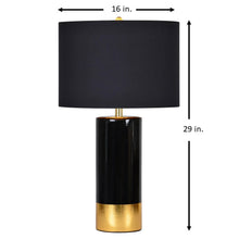Table lamp with black drum shade, glossy black stem, and gold metal base ring
