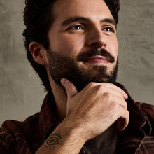 Man smoothing beard with balm on fingertips, trimmed mustache and beard