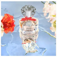 Amore eau de parfum glass bottle with ornate silver cap and red bow, against flowers