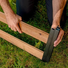Hands attaching a black corner bracket to a wooden raised garden bed panel