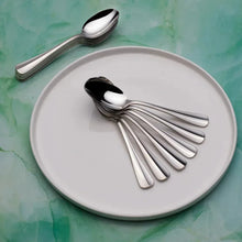 Polished silver teaspoons with dark bowls, arranged on a white plate