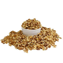 Chopped walnut pieces in a small bowl with loose pieces scattered around