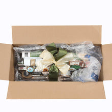 Packed gift basket assortment in open cardboard box with green and gold bows