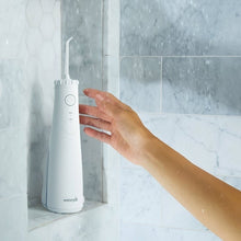 White cordless water flosser dispensing water stream, held at sink