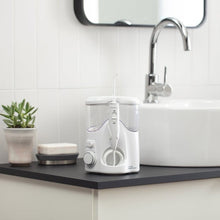 White countertop water flosser with removable nozzle and control buttons on a bathroom vanity.
