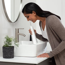 Person using a white cordless water flosser at the mouth in a bathroom.
