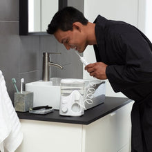 Person holding a cordless water flosser nozzle while using it at a sink.