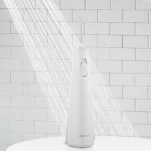 White cordless water flosser with nozzle and water spray stream against a tiled wall.