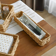 Rectangular rattan-style storage bin with woven handle, holding folded cutlery