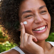 Weleda Skin Food cream dab on cheek; smiling woman with her finger applying it.