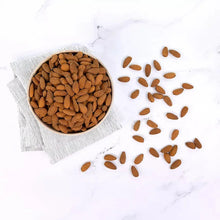 Raw almonds scattered with cloth and small pile in bowl