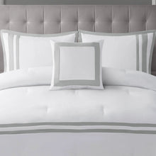 White comforter with gray striped band and decorative pillows on a bed.