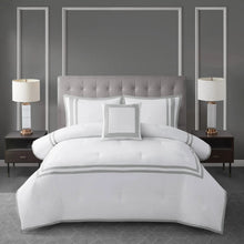 White comforter set with gray striped border, featuring shams and decorative pillows.