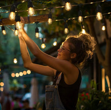 Warm white LED string lights with clear bulbs, being hung by a person