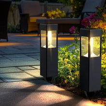Two black solar path lights with warm light in a garden walkway