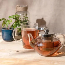 Glass teapot and cups with amber tea, with loose tea leaves nearby